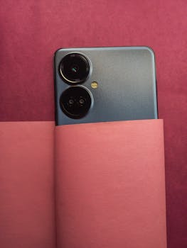 Close-up of a smartphone camera set against a pink paper backdrop, highlighting sleek design and technology.