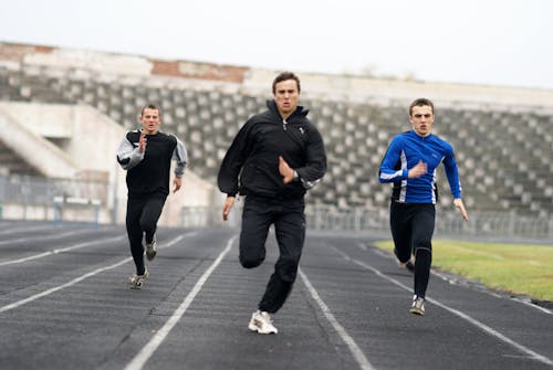 Three men running on a track in a stadium