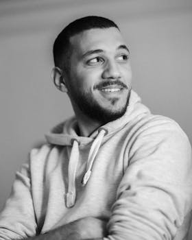 A casual black and white portrait of a smiling man wearing a hoodie, looking away.