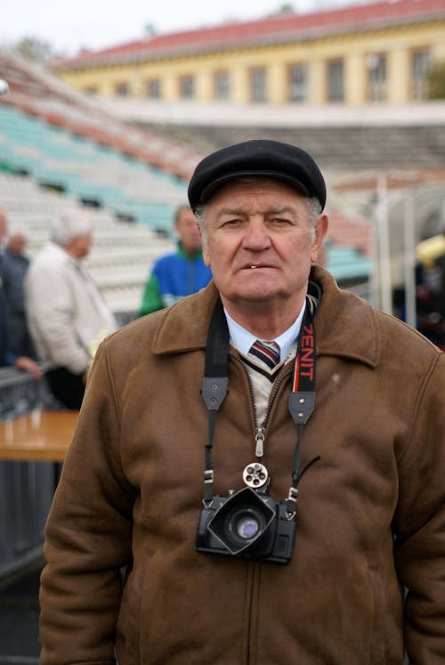 A man in a brown jacket and hat holding a camera