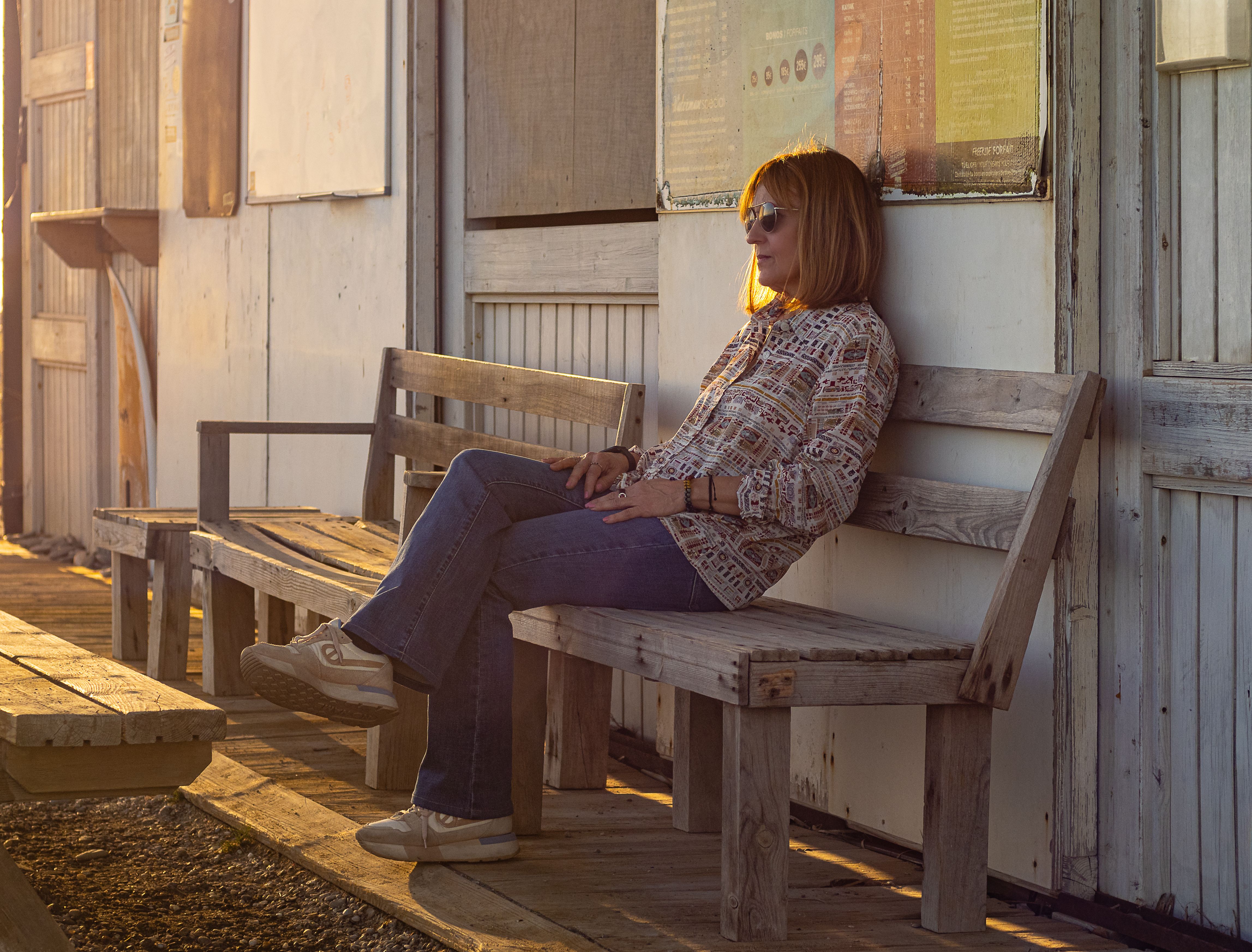 A woman sitting on a wooden bench in Motril, enjoying a sunny urban environment.