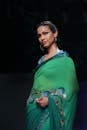 一位时尚女性身着充满活力的绿色纱丽，在T台上优雅地展现风采