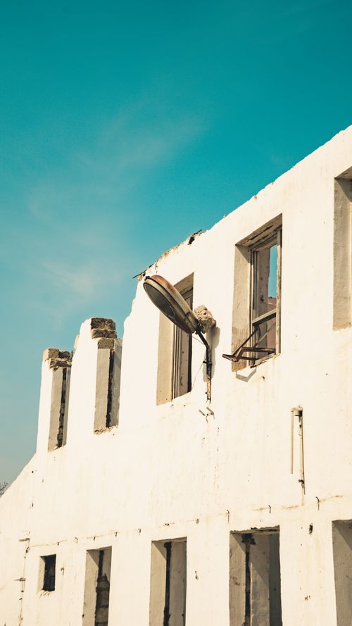 Free A damaged white building with broken windows under a clear sky, featuring a satellite dish. Stock Photo