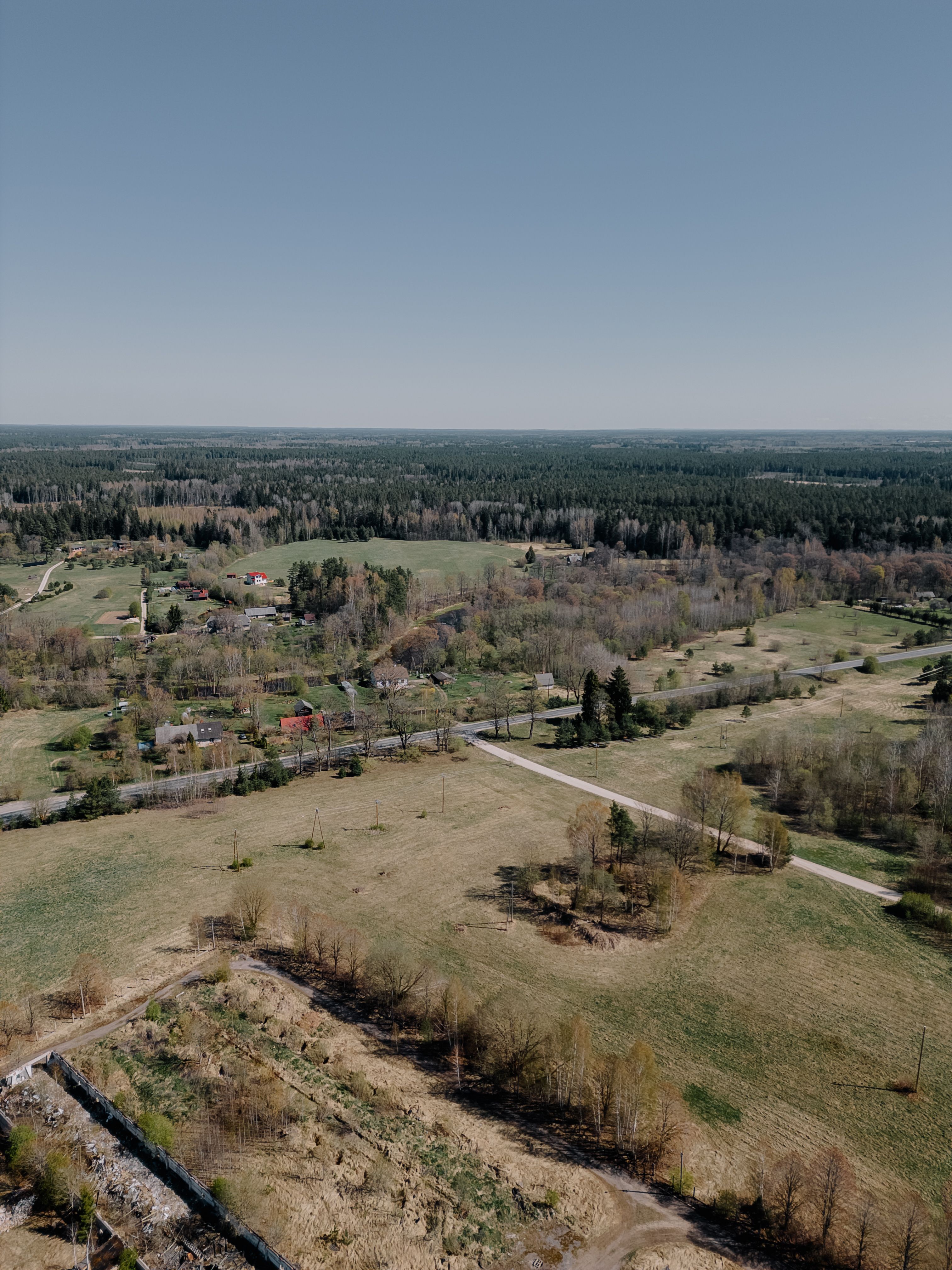 Expansive aerial shot of the serene countryside near Zaķumuiža, Latvia during a sunlit day.