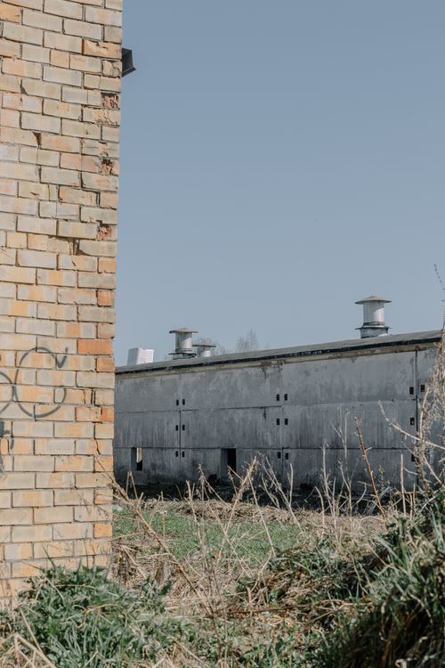 Free A gritty urban scene featuring a brick wall with graffiti and an industrial building under clear skies. Stock Photo