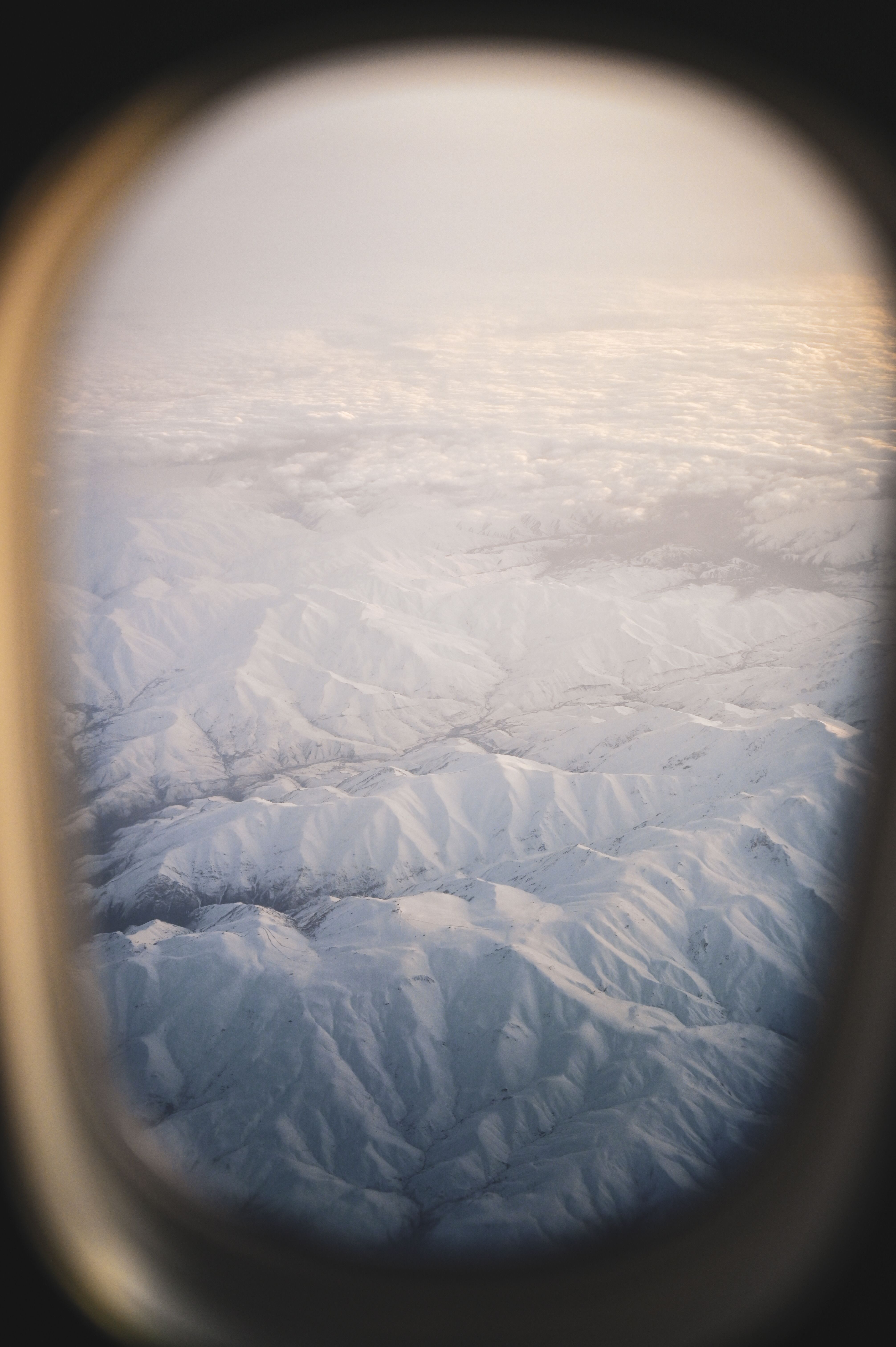 Capture of a snow-covered mountain range from an airplane window at sunrise, showcasing winter landscapes.