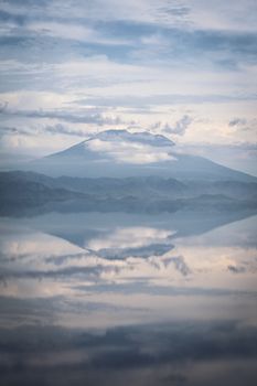 A serene mountain range reflected in a calm, misty lake creating a tranquil landscape view.