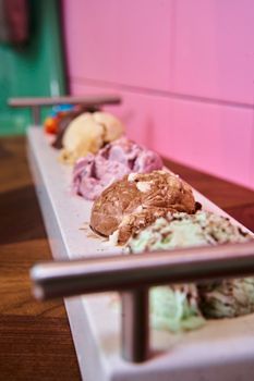 Colorful assortment of different ice cream scoops on a wooden tray with a pink background.