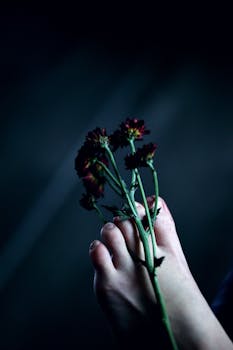 Close-up of toes holding dark flowers on a blurred dark background.
