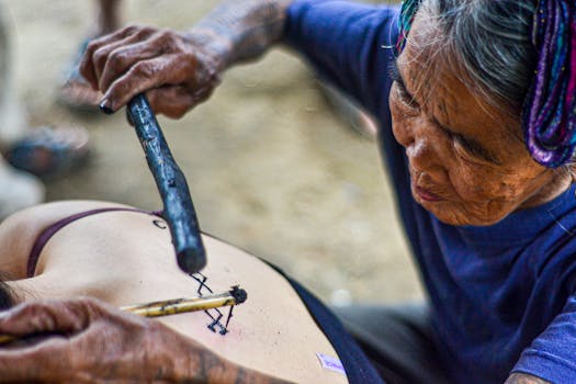Elderly woman performing traditional hand-tap tattooing on a younger person's back in Kalinga, Philippines.