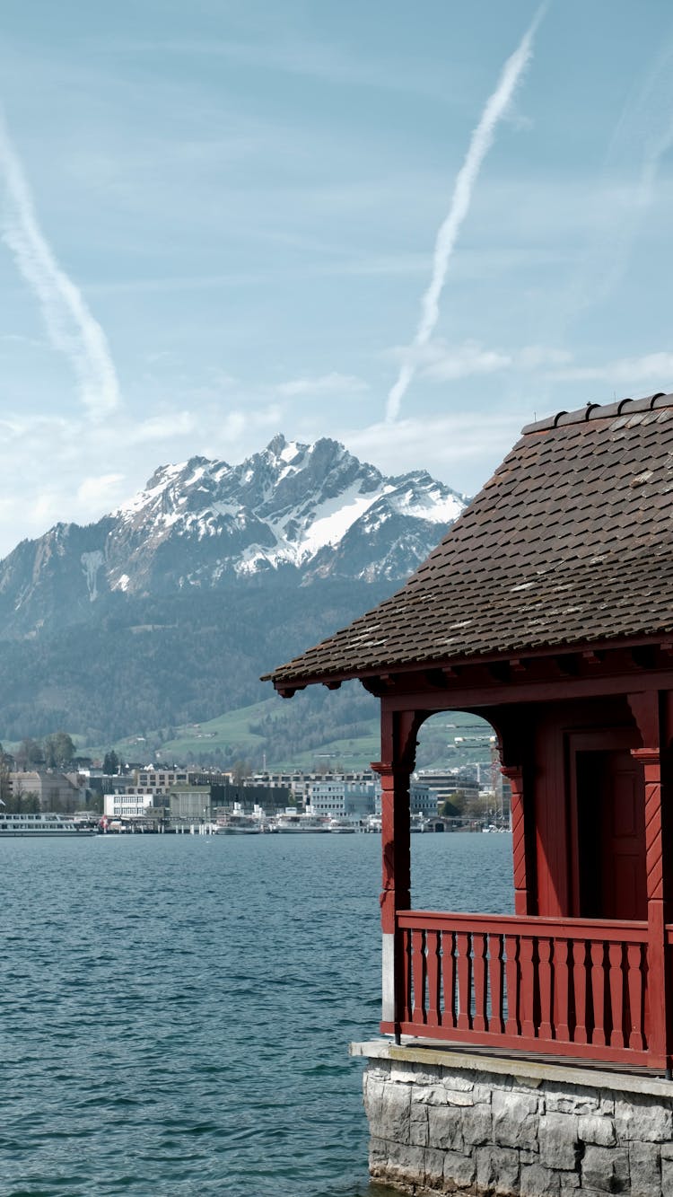 House On Riverbank With Town And Mountain Behind