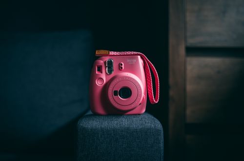 Free A vibrant pink instant camera sitting prominently against a moody backdrop, with a focus on its retro design. Stock Photo