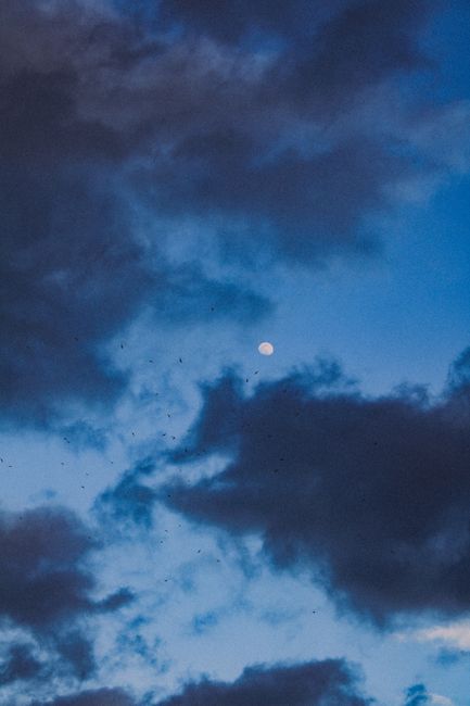 A captivating view of the moon amidst dramatic dark clouds in a vibrant blue sky.