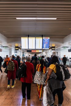 Travelers lining up in a busy airport terminal with baggage under flight information screens.