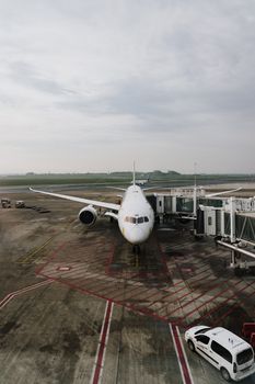 Front view of a commercial airplane parked at the airport gate on a cloudy day, ready for boarding.