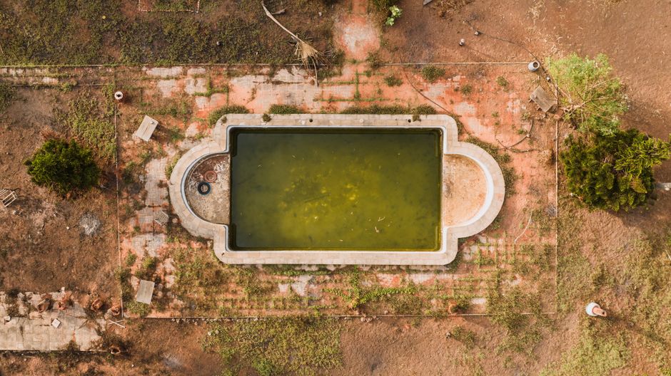 Aerial view of a neglected pool with stagnant green water and cracked surrounds, signalling leak damage.