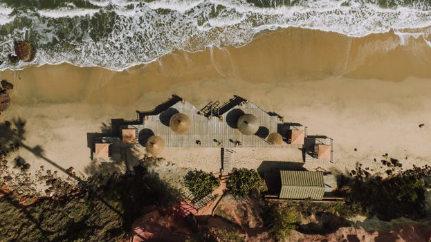 A breathtaking drone view of a sunlit beach with waves crashing against a wooden pier.