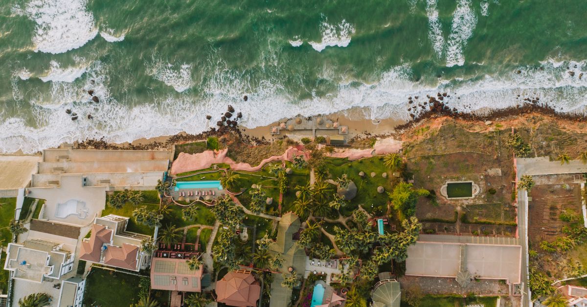 Stunning aerial view of beachfront homes with lush gardens and ocean waves in a coastal paradise.