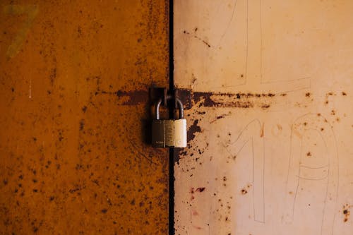 Free A close-up view of a rusty padlock securing a weathered metal door, highlighting decay and security. Stock Photo