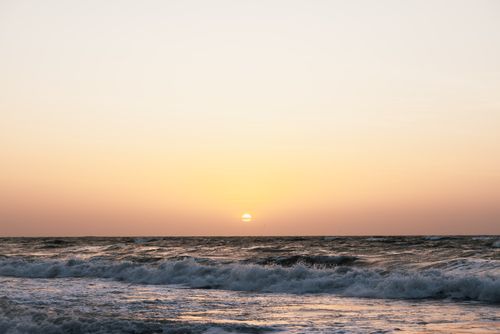 Free A breathtaking sunset over the ocean with waves crashing on the shore under a serene sky. Stock Photo