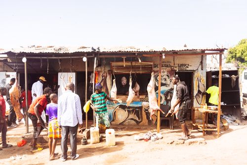 Free A bustling African village market displaying hanging meat and local interactions. Stock Photo