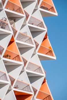 Close-up of a modern geometric apartment building in Dubai with orange accents and a clear blue sky.