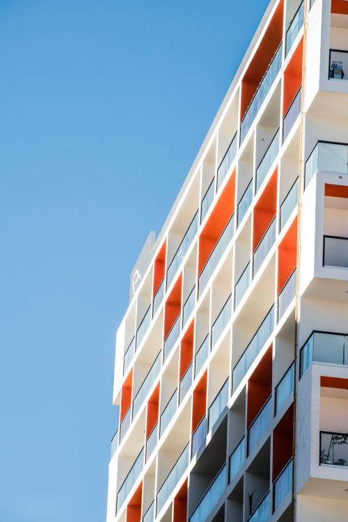 Free Minimalist apartment complex in Dubai with orange accents against a clear blue sky. Stock Photo