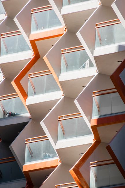 Close-up of a modern geometric building facade in Dubai, featuring glass balconies and orange accents.