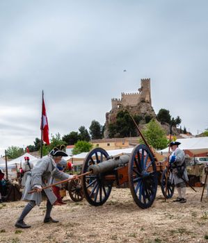Soldiers in period uniforms operate a cannon during a reenactment near a historic castle.