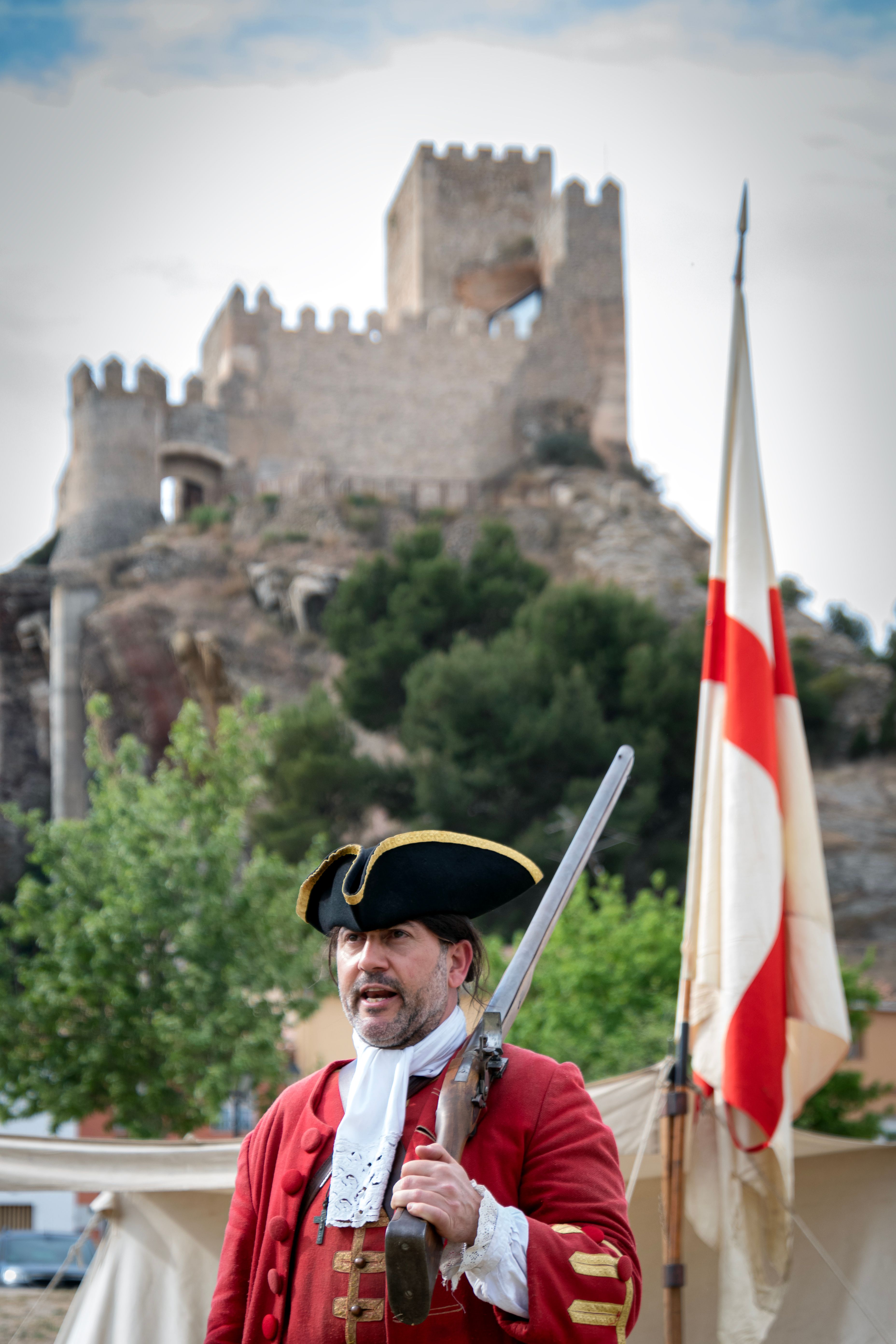 Man in historical uniform posing with musket near a medieval castle.