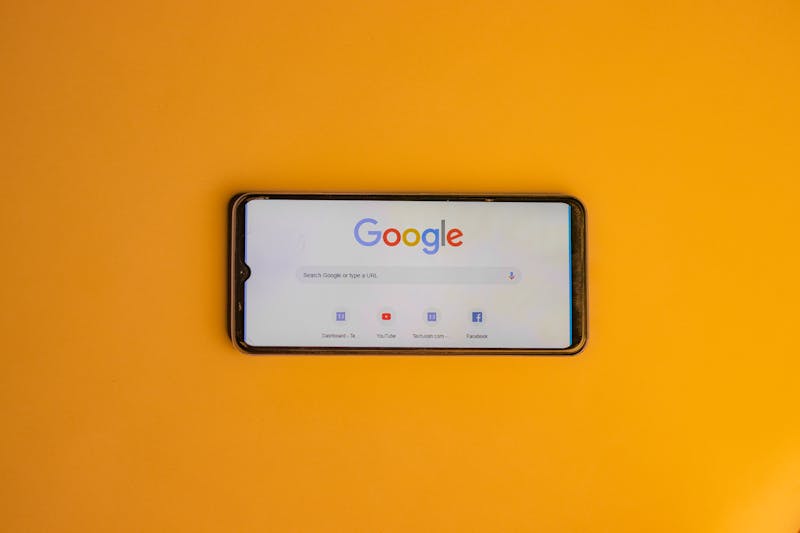 Smartphone displaying Google search page on a vibrant yellow background.