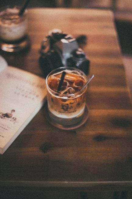 Cozy coffee shop scene with iced coffee, book, and vintage camera on wooden table.