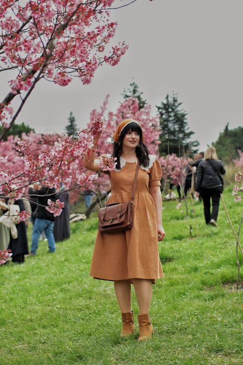 Young Woman in a Dress Standing in a Park next to Cherry Blossom 
