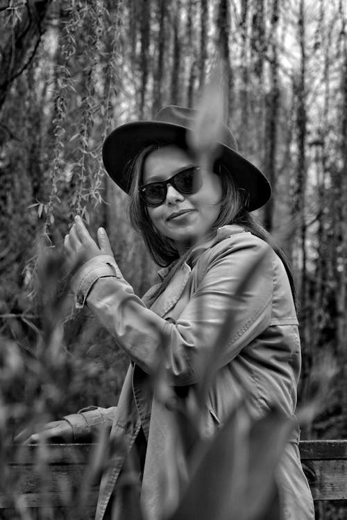 Woman Posing in Hat and Sunglasses among Trees in Black and White