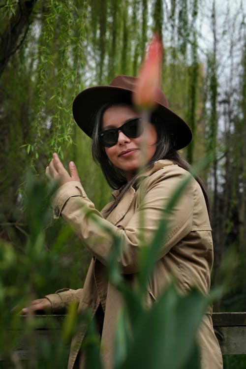 Young Woman Wearing a Trench Coat and Sunglasses in a Park 