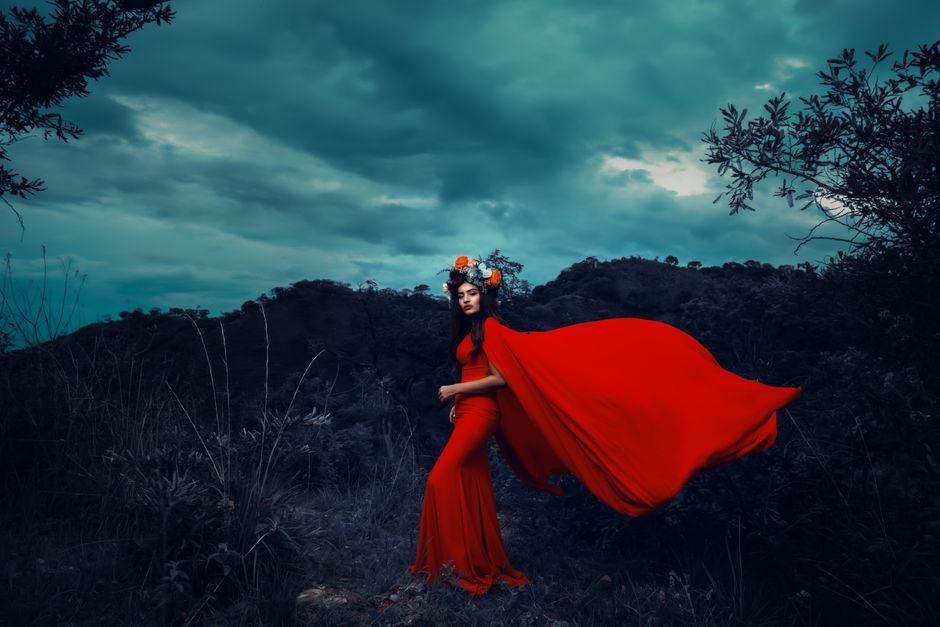 A striking image of a woman in a flowing red dress against a moody backdrop of storm clouds.