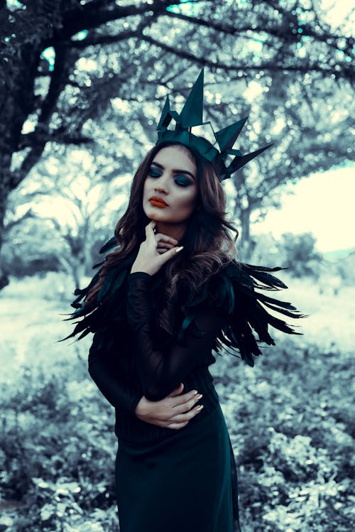 Young Woman in a Black Costume and a Crown Posing Outdoors 