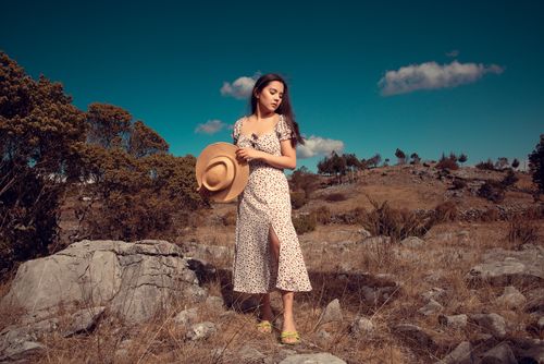 Free Young woman in a floral dress and hat standing in a rocky landscape. Stock Photo