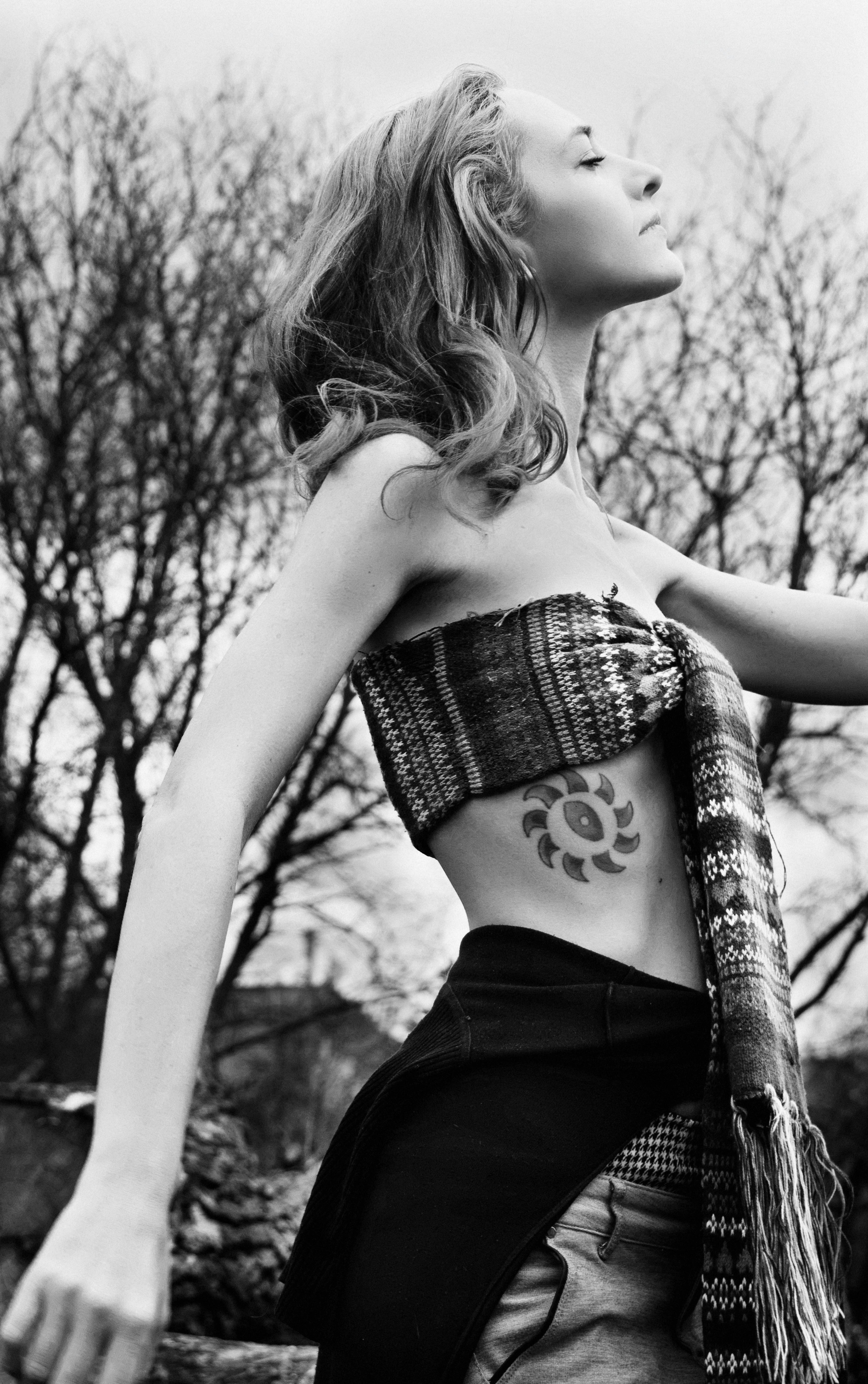 Artistic black and white portrait of a woman embracing nature with closed eyes and visible tattoo.
