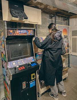 A woman explores vinyl records next to a vintage arcade machine in a retro music store.