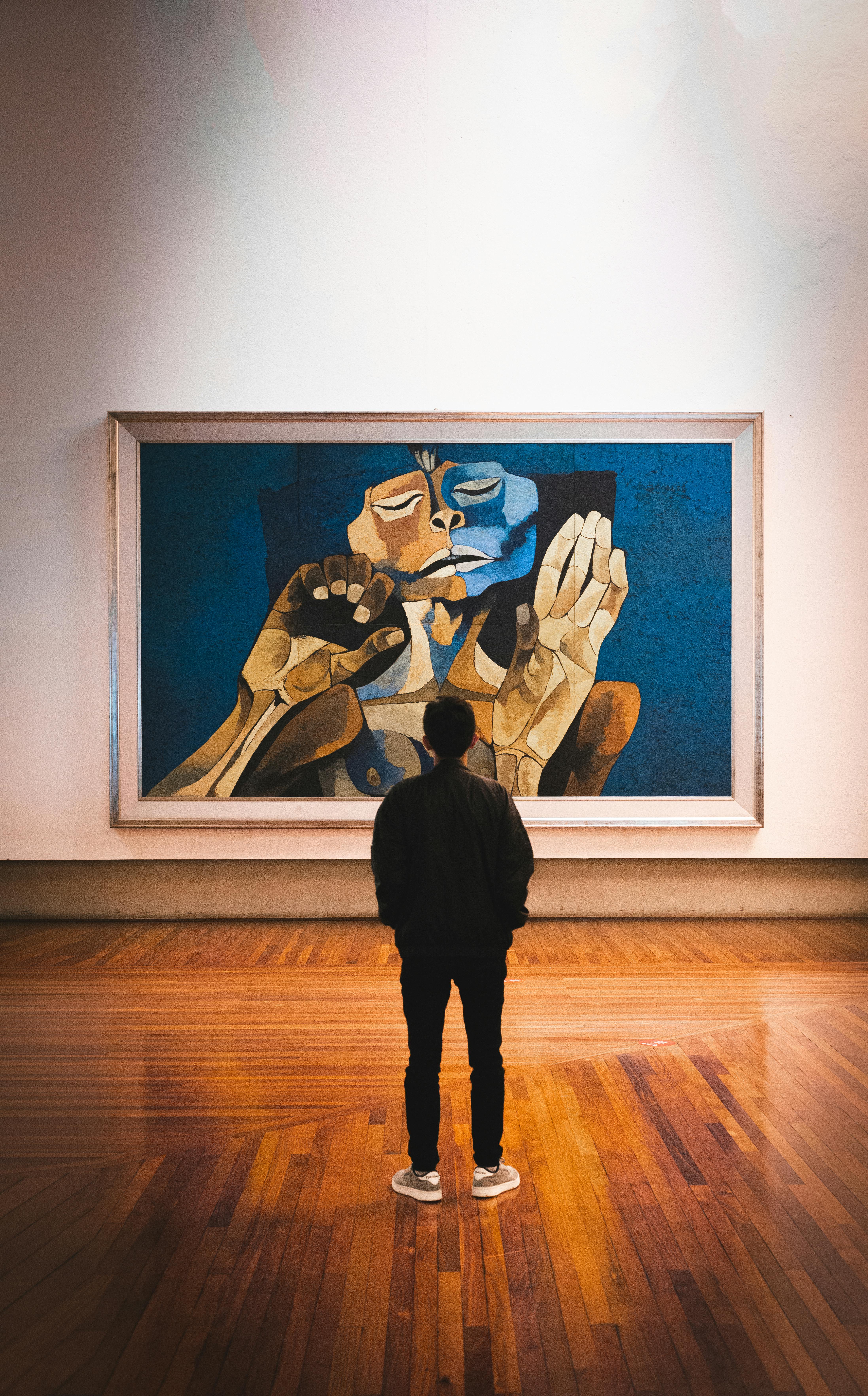 A man stands admiring an abstract painting in a gallery, highlighting cultural appreciation.