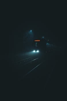 Atmospheric nighttime shot of a tram on foggy city streets, featuring headlights cutting through the dark.