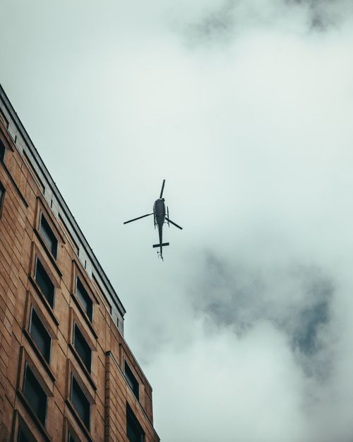 Free A cityscape with a helicopter flying above a building against a cloudy sky, offering a dynamic urban view. Stock Photo