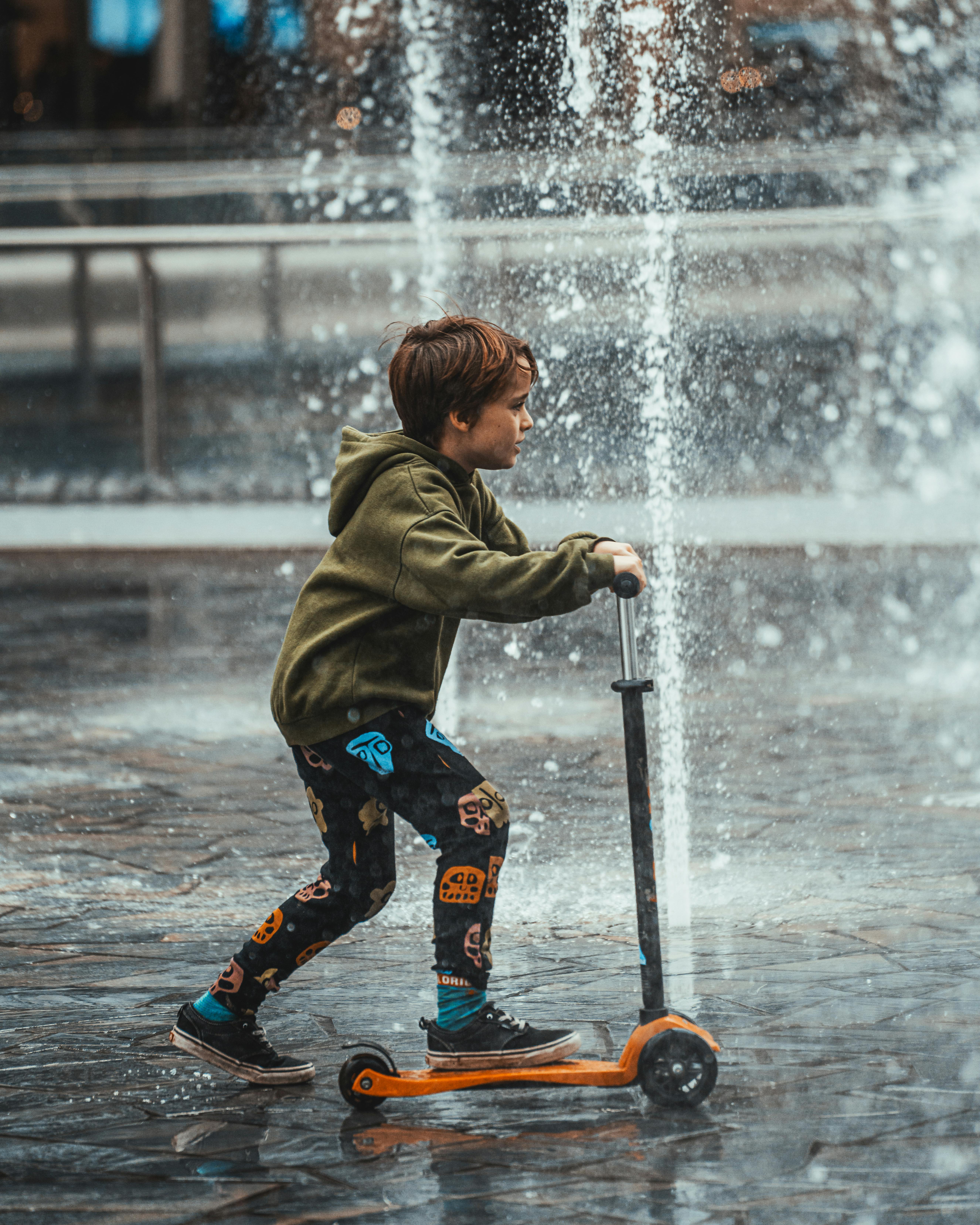 boy riding scooter under fountain water