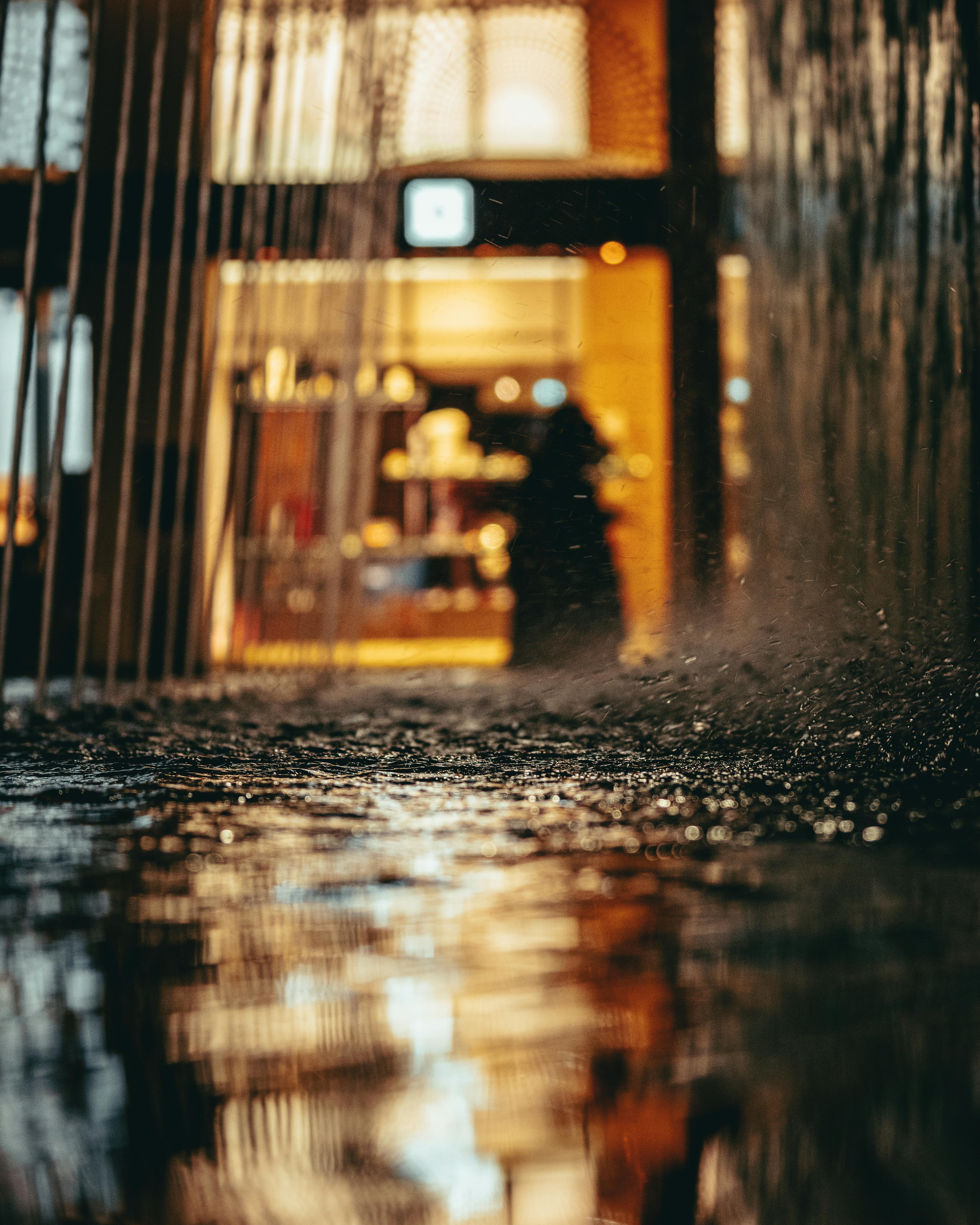 A rainy evening scene with reflections and warm light from a building.