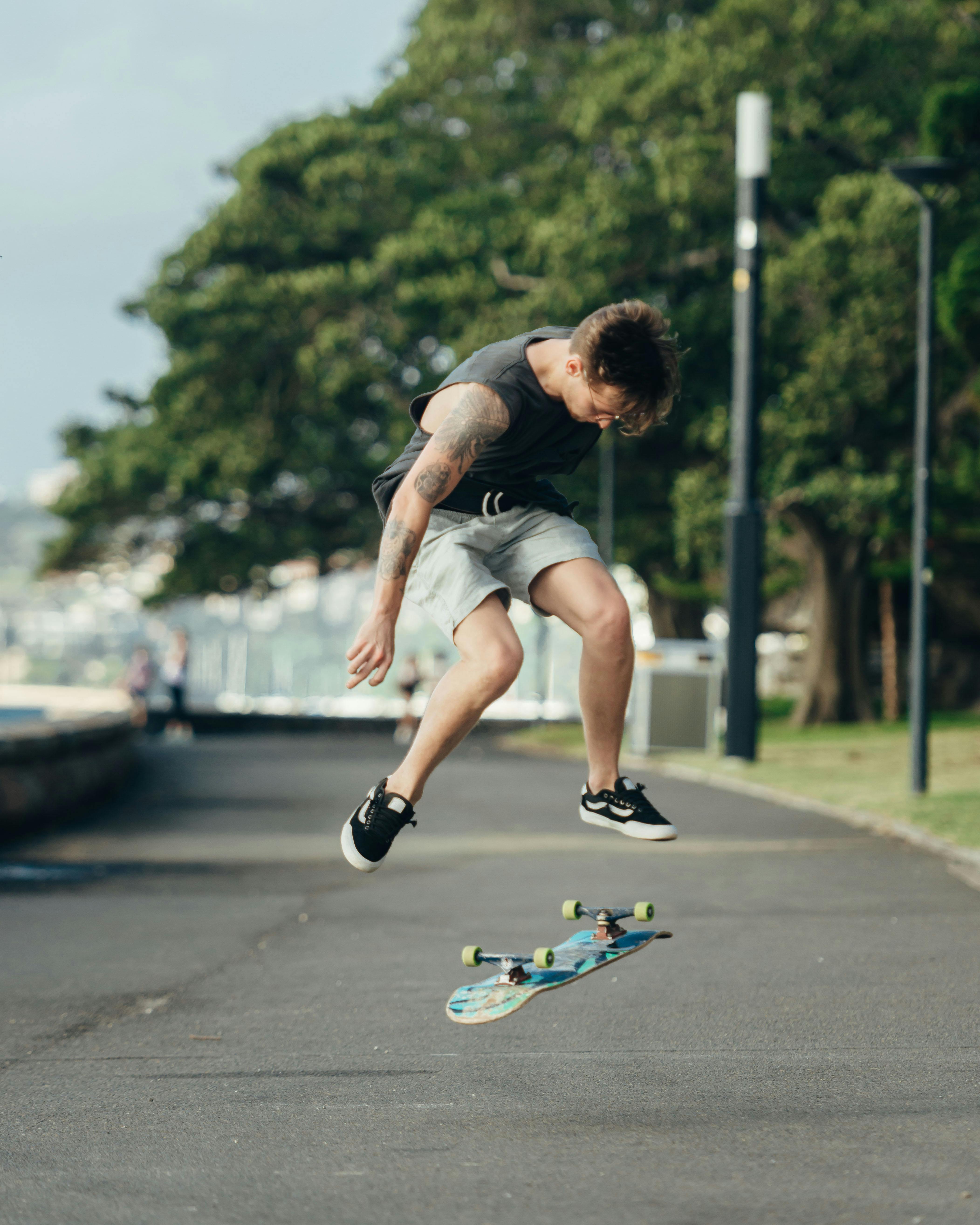 Man in Black Tank Top on Road Doing Skateboard Tricks