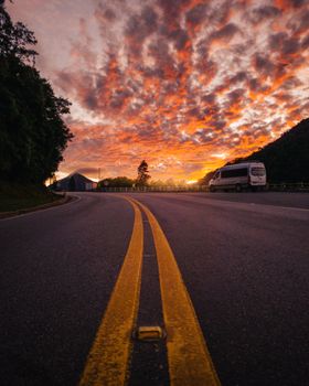 A serene curved road leading into a colorful sunset, under a sky filled with dramatic clouds.