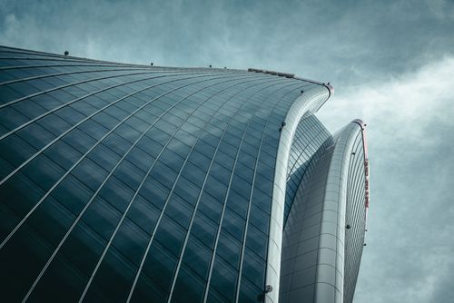 Free Low angle view of a modern skyscraper featuring a striking curved glass facade against an overcast sky. Stock Photo