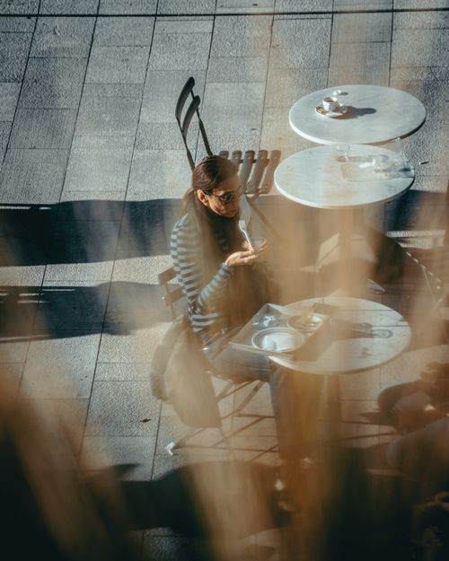 Free A stylish woman enjoys coffee at an outdoor café table, capturing urban city life. Stock Photo