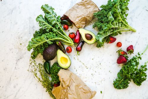 Free Avocado, kale, and more fresh produce artfully arranged on a marble surface. Stock Photo